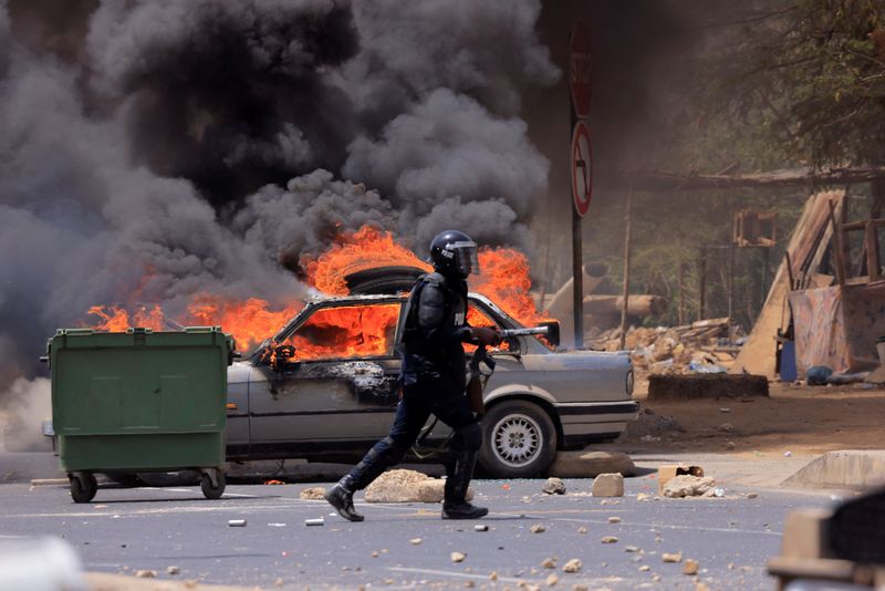 &copy; Reuters. أحد أفراد شرطة مكافحة الشغب يسير بالقرب من سيارة مشتعلة خلال اشتباكات بين أنصار زعيم المعارضة السنغالي عثمان سونكو وقوات الأمن بعد الحكم عل