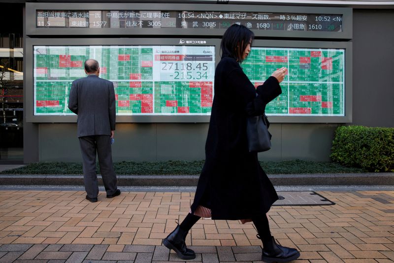 &copy; Reuters. FILE PHOTO: A woman walks past a man examining an electronic board showing Japan's Nikkei average and stock quotations outside a brokerage, in Tokyo, Japan, March 20, 2023. REUTERS/Androniki Christodoulou