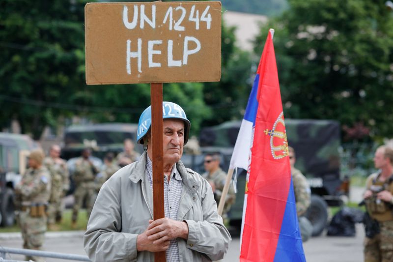 &copy; Reuters. A person holds a placard as members of the NATO-led Kosovo Force (KFOR) stand guard outside municipal offices in Leposavic, Kosovo, June 2, 2023. REUTERS/Ognen Teofilovski