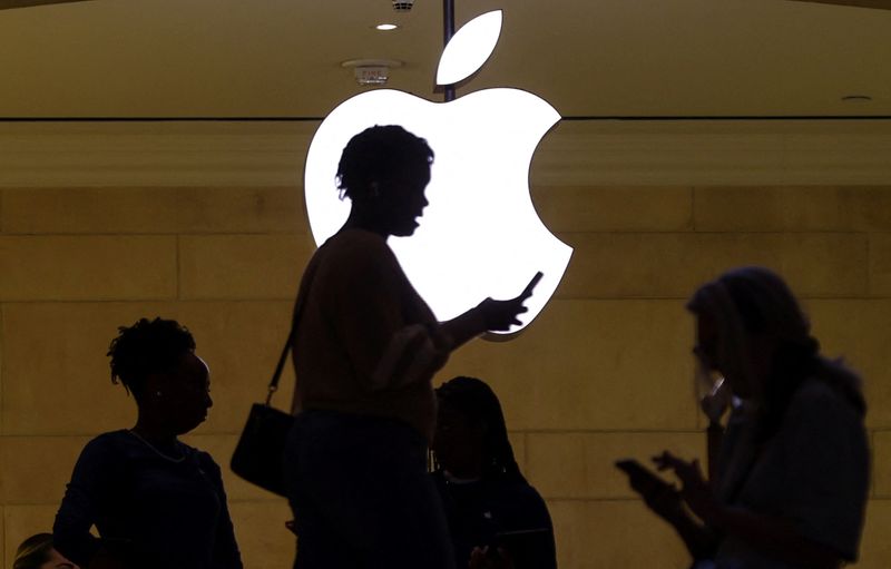 © Reuters. FILE PHOTO: A women uses an iPhone mobile device as she passes a lighted Apple logo at the Apple store at Grand Central Terminal in New York City, U.S., April 14, 2023. REUTERS/Mike Segar