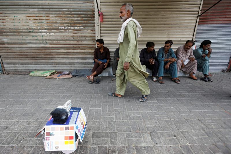 &copy; Reuters. FILE PHOTO: Men, who work as painters, wait for work next to closed shops in Karachi, Pakistan June 10, 2022. REUTERS/Akhtar Soomro