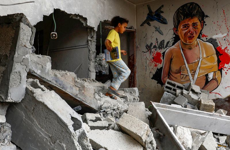 &copy; Reuters. فتاة فلسطينةي تسير جوار  رسمة لفتى يبكي على جدار منزل مهدوم جراء الهجمات الإسرائيلية بقطاع غزة في الثامن من يونيو حزيران 2023. تصوير: إبراهيم ا