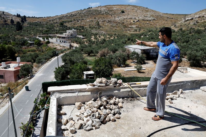 &copy; Reuters. فلسطيني على سطح منزله وبجواره كومة من الحجارة بعد هجمات مستوطنين على قرية برقة بالضفة الغربية المحتلة في صورة بتاريخ السابع من يونيو حزيران