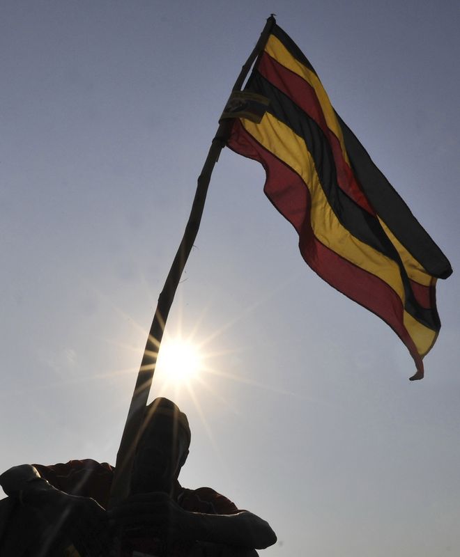 &copy; Reuters. Un homme à côté du drapeau national ougandais à Kampala, la capitale du pays. /Photo prise le 16 février 2011/REUTERS/James Akena