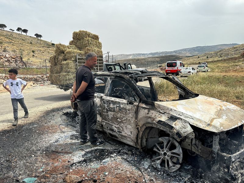 &copy; Reuters. فلسطينيون يقفون إلى جانب سيارة متفحمة بعد أن أحرقها مستوطنون إسرائيليون خلال اشتباكات بالقرب من رام الله بالضفة الغربية المحتلة يوم 26 مايو 