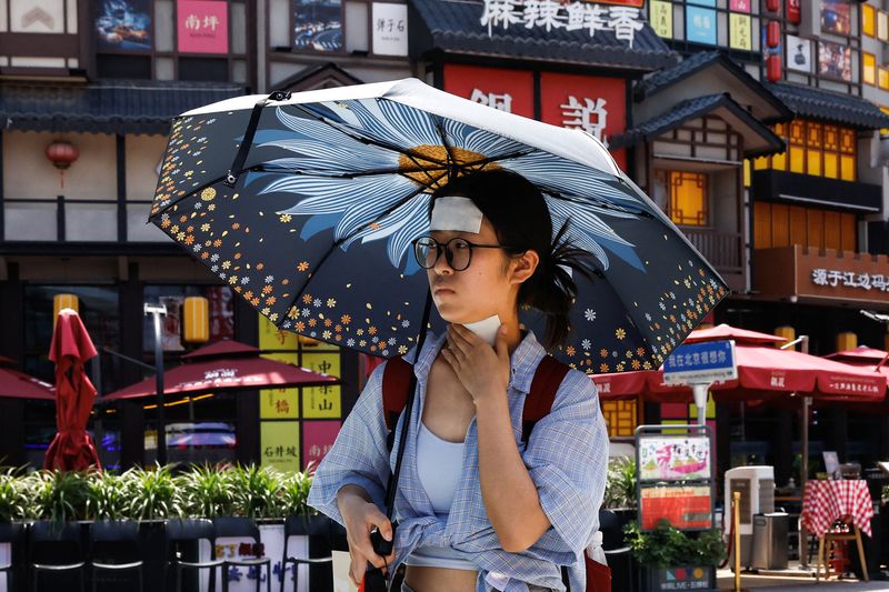 &copy; Reuters. A woman walks with cold patches on her forehead and neck amid a red alert for heatwave in Beijing, China June 23, 2023. REUTERS/Tingshu Wang