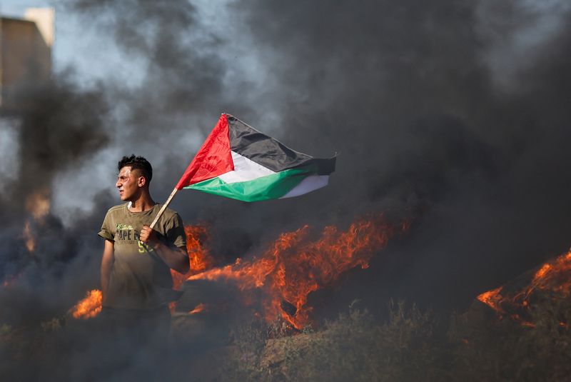 &copy; Reuters. فلسطيني يحمل العلم الفلسطيني على الشريط الحدودي بين قطاع غزة وإسرائيل يوم الاثنين خلال مشاركته في احتجاج ضد العملية العسكرية الإسرائيلية ف