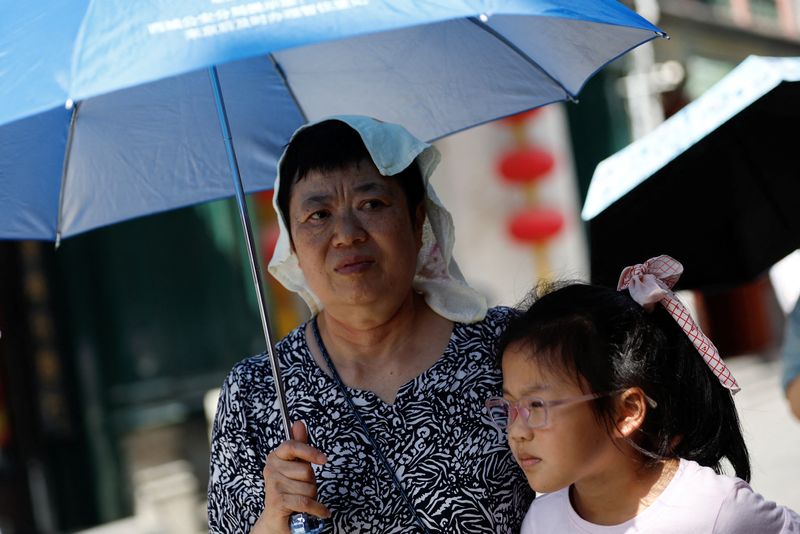 © Reuters. A person wearing a towel on her head holds an umbrella, as she walks on a street, amid a red alert for heatwave in Beijing, China July 6, 2023. REUTERS/Tingshu Wang