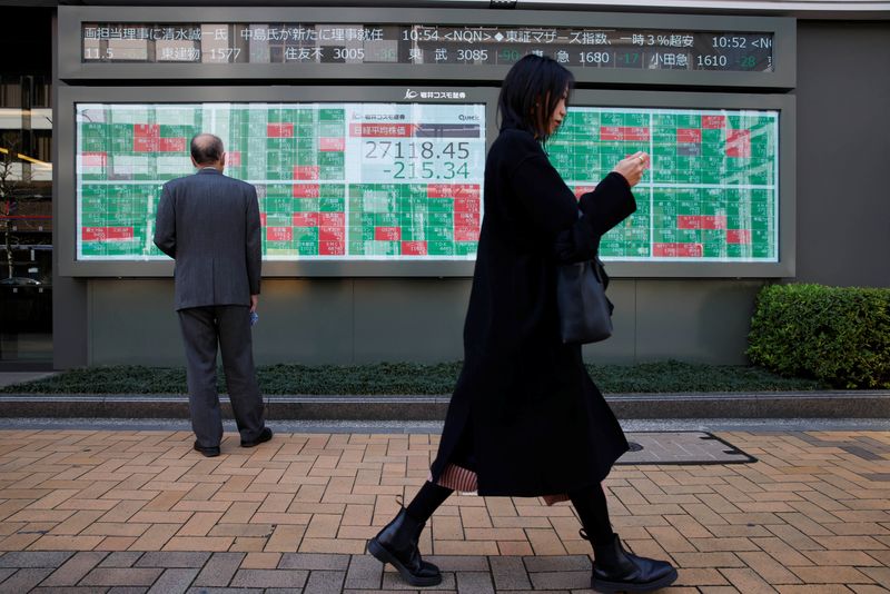 &copy; Reuters. امرأة تسير بالقرب من رجل يقف أمام شاشة إلكترونية تعرض حركة مؤشر نيكي الياباني وأسعار الأسهم خارج مكتب للسمسرة في طوكيو يوم 20 مارس آذار 2023. تص