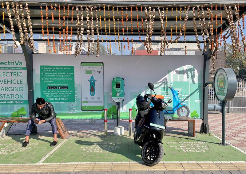 &copy; Reuters. FILE PHOTO: A man checks his mobile phone as he waits while recharging his Ola electric scooter at an electric vehicle charging station in New Delhi, India, February 12, 2022. Picture taken February 12, 2022. REUTERS/Aditi Shah/File Photo