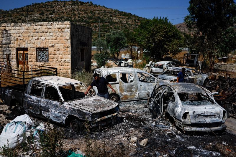© Reuters. شابان فلسطينيان يفحصان بعض السيارات المحترقة جراء هجمات نفذها مستوطنون يهود بالقرب من رام الله بالضفة الغربية المحتلة في 21 يونيو حزيران 2023 . تصوير : عمار عوض - ر ويترز .   