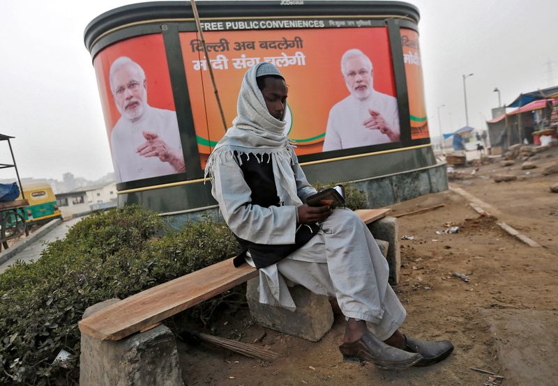 &copy; Reuters. Muçulmano lê Alcorão em frente a um outdoor com o primeiro-ministro da Índia, Narendra Modi, em Nova Délhi
 20/1/2015   REUTERS/Adnan Abidi