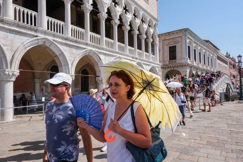 &copy; Reuters. سياح يحتمون من أشعة الشمس في ساحة سان مارك في فينيسيا  بإيطاليا يوم السبت. تصوير: مانويل سيلفستري - رويترز