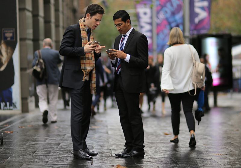 &copy; Reuters. FILE PHOTO: Businessmen use their phones as they stand in the central business district (CBD) of Sydney in Australia, May 14, 2017. Picture taken May 14, 2017.  REUTERS/Steven Saphore