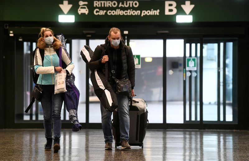 &copy; Reuters. FILE PHOTO: People wearing protective masks walk in Malpensa airport near Milan, Italy, March 9, 2020. REUTERS/Flavio Lo Scalzo