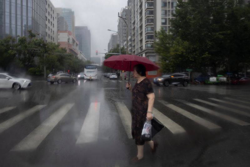 © Reuters. امرأة تعبر الشارع أثناء هطول أمطار غزيرة في بكين يوم السبت. تصوير: توماس بيتر - رويترز. 