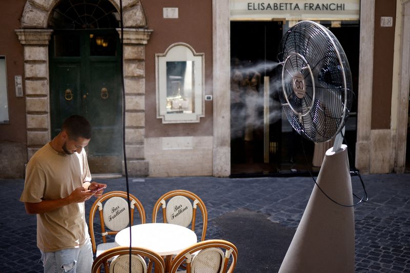 © Reuters. FILE PHOTO: A man checks his phone as he stands near a fan to cool off during a heatwave across Italy, in Rome, July 14, 2023. REUTERS/Guglielmo Mangiapane/File Photo