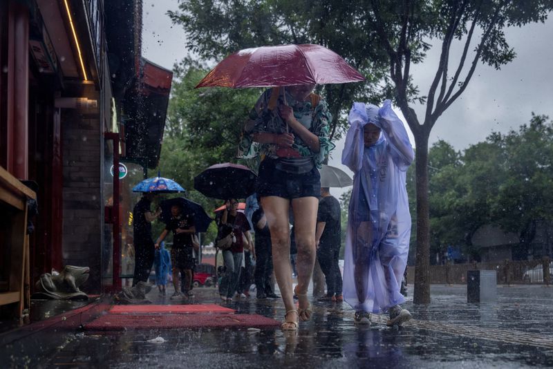&copy; Reuters. Persone con indosso un impermeabile si riparano sotto l'ombrello in una zona turistica della città durante una forte pioggia a Pechino, Cina, 30 luglio 2023. REUTERS/Thomas Peter