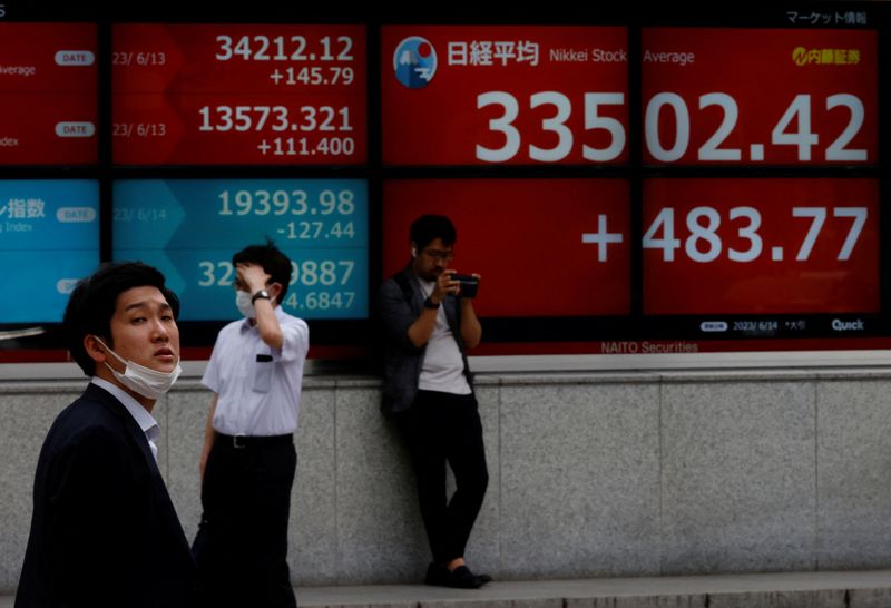 © Reuters. رجال يقفون أمام لوحة إلكترونية تعرض حركة تداول الأسهم على مؤشر نيكي الياباني خارج شركة للسمسرة في طوكيو في 14 يونيو حزيران 2023 . تصوير : كيم كيونج هون - رويترز . 