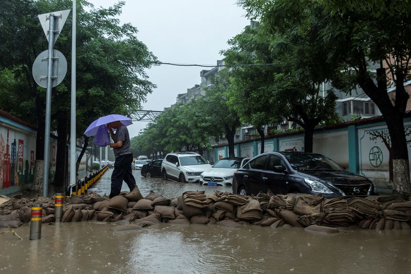 © Reuters. رجل يعبر الشارع فوق أكياس رملية يوم الثلاثاء بسبب الفيضانات الناجمة عن الأمطار الغزيرة التي شهدتها العاصمة الصينية بكين بسبب إعصار دوكسوري . تصوير : توماس بيتر - رويترز .    