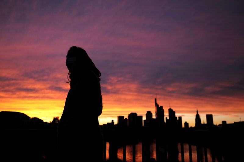 &copy; Reuters. FILE PHOTO: A woman wearing a protective mask walks past the skyline of the financial district during sunset as the spread of the coronavirus disease (COVID-19) continues in Frankfurt, Germany, October 26, 2020, REUTERS/Kai Pfaffenbach/File Photo  