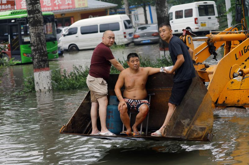 © Reuters. People stand on a front loader travelling through floodwaters after the rains and floods brought by remnants of Typhoon Doksuri, in Zhuozhou, Hebei province, China August 3, 2023. REUTERS/Tingshu Wang