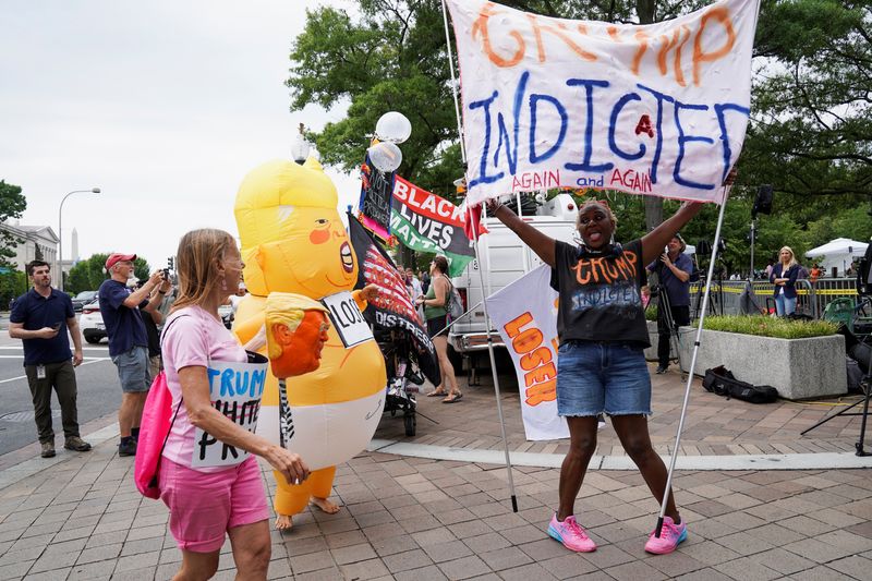 &copy; Reuters. A demonstrator holds a banner, while standing near a person wearing a Baby Trump costume, as people gather on the day former U.S. President Donald Trump, who is facing federal charges related to attempts to overturn his 2020 election defeat, appears at th