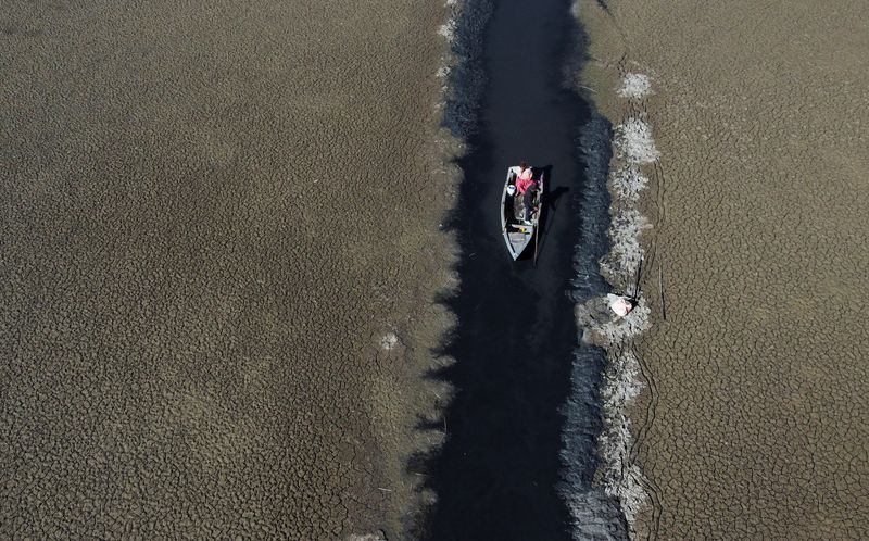 © Reuters. Isabel Apaza and Gabriel Flores sail in their boat through a narrow water path near the shore of Lake Titicaca in drought season in Huarina, Bolivia August 3, 2023. REUTERS/Claudia Morales