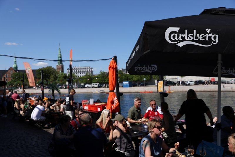 &copy; Reuters. FILE PHOTO: People sit under signage for Carlsberg beer at a terrace in Copenhagen, Denmark, July 30, 2022. REUTERS/Andrew Kelly/File Photo