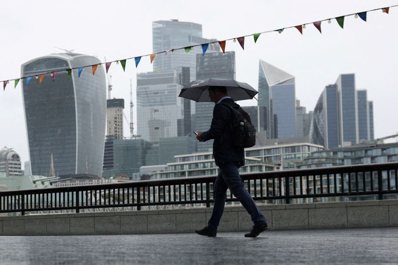 &copy; Reuters. FILE PHOTO: A pedestrian carrying an umbrella walks along the River Thames in view of City of London skyline in London, Britain, July 31, 2023. REUTERS/Hollie Adams/File Photo