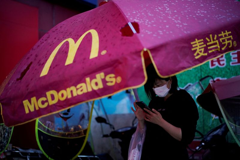 &copy; Reuters. FILE PHOTO: A woman wearing a face mask checks her mobile phone under an umbrella with a McDonald's sign in Xianning of Hubei province, the epicentre of China's coronavirus disease (COVID-19) outbreak, March 25, 2020. REUTERS/Aly Song/File Photo
