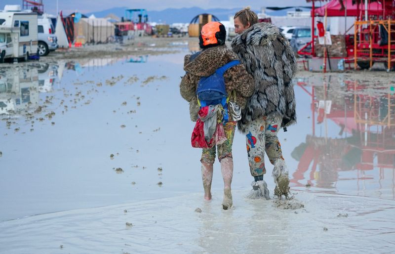 © Reuters. Dub Kitty and Ben Joos, of Idaho and Nevada, walk through the mud at Burning Man after a night of dancing with friends in Black Rock City, in the Nevada desert, after a rainstorm turned the site into mud September 2, 2023.  Trevor Hughes/USA TODAY NETWORK via REUTERS  