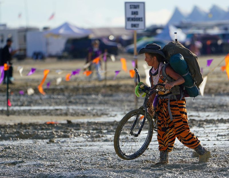 © Reuters. A Burning Man participant walks their bike through the mud near the exit, after a severe rainstorm left tens of thousands of revelers attending the annual festival stranded in mud in Black Rock City, in the Nevada desert September 3, 2023.  Trevor Hughes/USA Today Network via REUTERS
