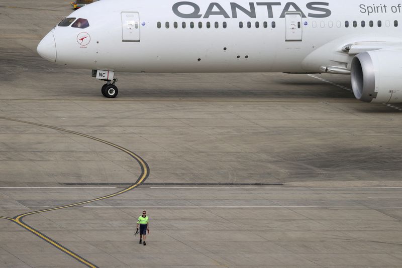 © Reuters. FILE PHOTO: FILE PHOTO: A ground worker walking near a Qantas plane is seen from the international terminal at Sydney Airport in Australia, November 29, 2021.  REUTERS/Loren Elliott/file photo/File Photo/File Photo