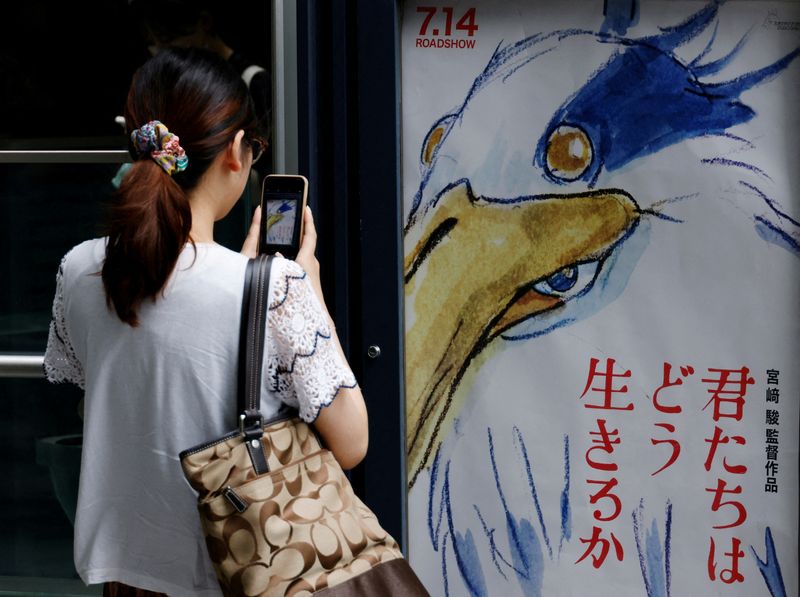 © Reuters. FILE PHOTO: A woman takes a picture of a movie poster for Oscar-winning Japanese animation master Hayao Miyazaki's film 