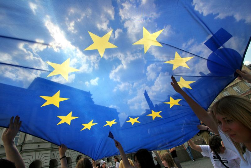 &copy; Reuters. Persone con una bandiera dell'Unione Europea durante una parata dell'UE nel centro di Varsavia, 13 maggio 2006.