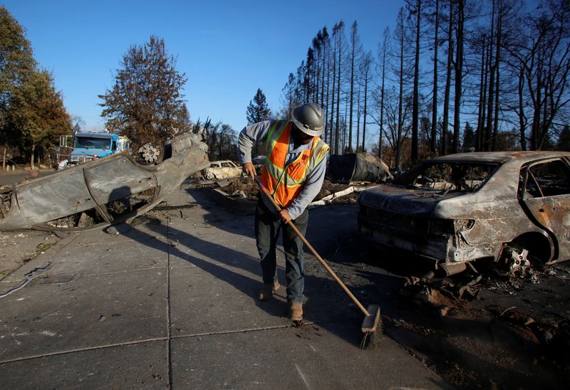 &copy; Reuters. An employee of Pacific Gas & Electric (PG&E) sweeps the sidewalk in a destroyed neighborhood after a wildfire tore through Santa Rosa, California, U.S., October 15, 2017. REUTERS/Jim Urquhart/File Photo