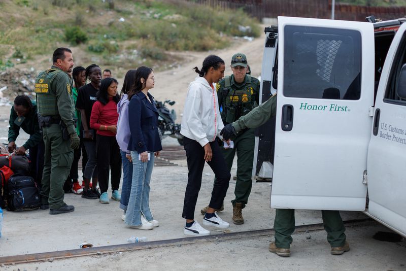 &copy; Reuters. Migrantes que se habían reunido entre las vallas fronterizas primaria y secundaria entre México y Estados Unidos son subidos a una furgoneta por la aduana y la patrulla fronteriza estadounidenses para ser procesados por inmigración en San Diego, Estado
