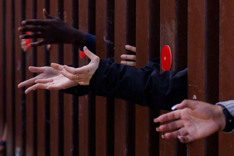 © Reuters. Migrants reach out from the border wall for food from an aid agency as the wait between the primary and secondary border fences.  California, U.S., May 11, 2023. REUTERS/Mike Blake/File photo