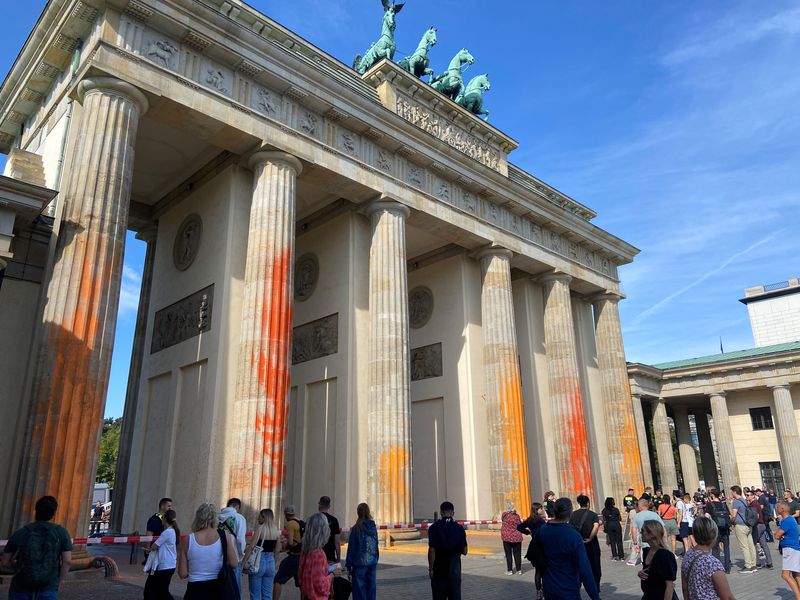&copy; Reuters. أشخاص يسيرون أمام بوابة براندنبورج الشهيرة في العاصمة الألمانية برلين بعد أن رش نشطاء معنيون بالمناخ أعمدة البوابة بطلاء برتقالي وأصفر يوم