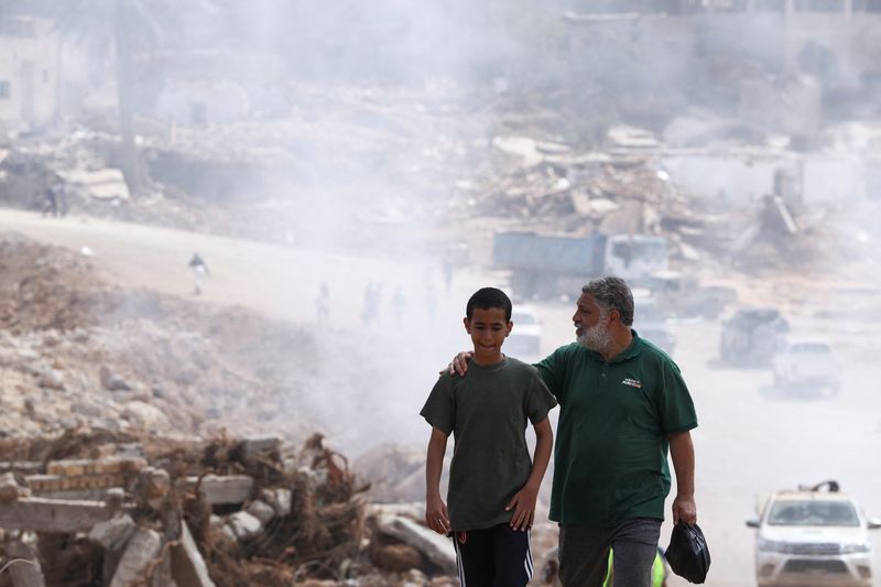 © Reuters. A father walks with his son with smoke caused by a sanitation truck visible in the background amid rising concerns of the spread of infectious diseases after fatal floods in Derna, Libya, September 18, 2023. REUTERS/Amr Alfiky