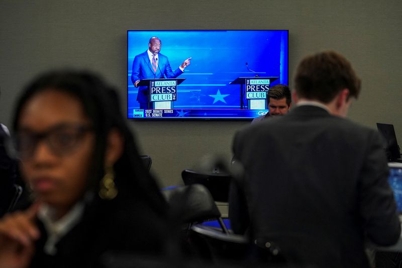 © Reuters. FILE PHOTO: U.S Senator Raphael Warnock gestures while he stands next to an empty podium representing his Republican challenger Herschel Walker, on a television screen, while participating in a debate at the Georgia Public Broadcasting offices in Atlanta, Georgia, U.S. October 16, 2022. REUTERS/Elijah Nouvelage