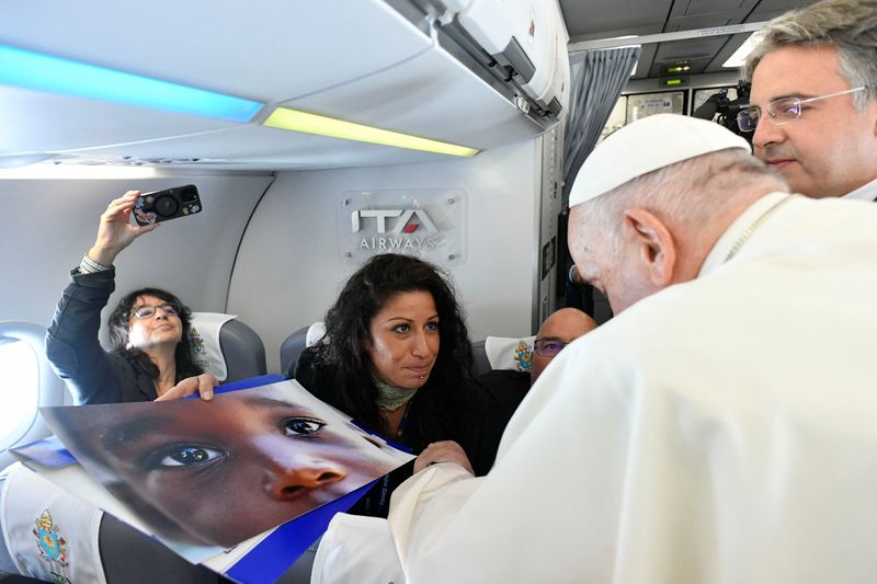 © Reuters. Reuters photographer Yara Nardi shows Pope Francis the photo of a child from Cameroon that she took at a reception center for irregular migrants on the Sicilian island of Lampedusa on September 15, 2023, during a trip on the occasion of the Mediterranean Meetings (MED 2023) in France, aboard the plane, September 22, 2023.    Vatican Media/Handout via REUTERS
