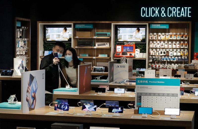 &copy; Reuters. FILE PHOTO: People wearing protective masks look at phones at an electronic retailer in Beijing, China March 25, 2020. REUTERS/Thomas Peter/File Photo