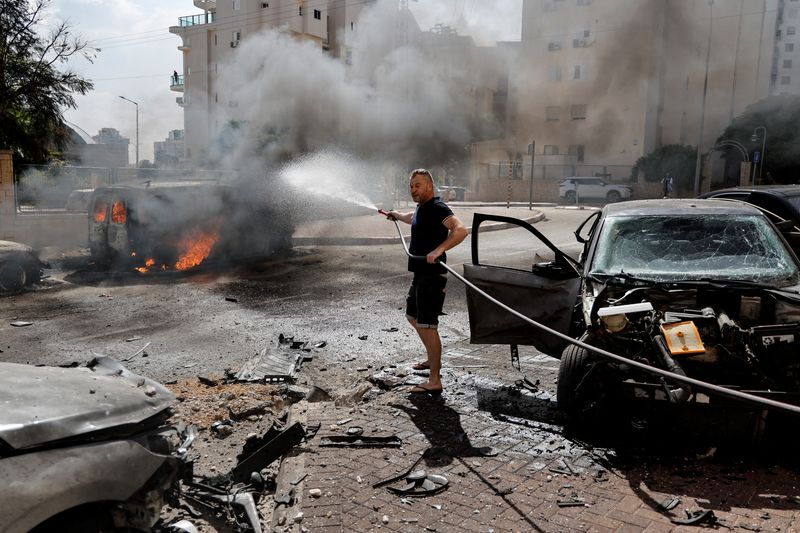 © Reuters. رجل يحاول اطفاء سيارة في عسقلان احترقت لدى إطلاق صواريخ من قطاع غزة يوم السبت. تصوير: عمار عوض - رويترز