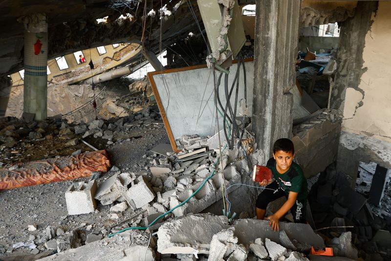 &copy; Reuters. طفل يحمل كتابا فيما يتفقد فلسطينيون الدمار الذي لحق بمسجد في خان يونس بقطاع غزة يوم الأحد. تصوير: إبراهيم ابو مصطفى - رويترز.