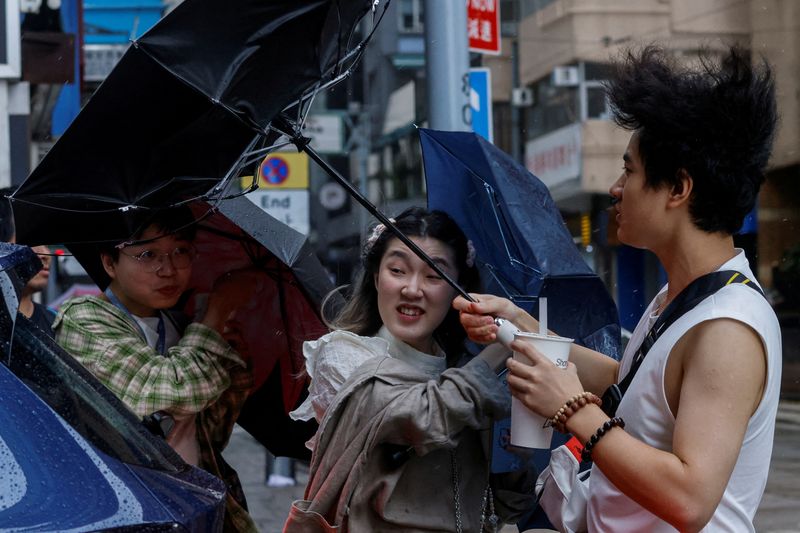 &copy; Reuters. أشخاص يحاولون الإمساك بمظلاتهم في مواجهة الرياح القوية بسبب تعرض هونج كونج لبقايا الإعصار كوينو يوم الأحد . تصوير : تيرون سيو - رويترز .   