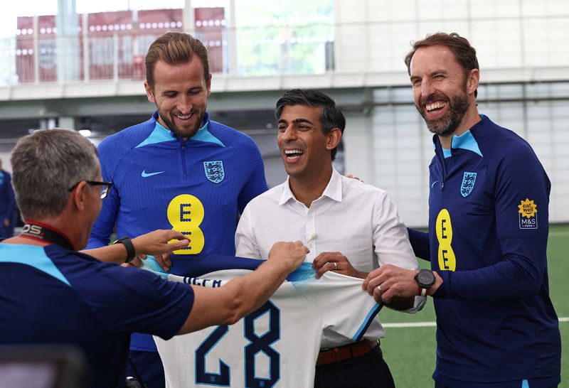 &copy; Reuters. A photographer directs Britain's Prime Minister Rishi Sunak in how to pose with an England football shirt, as he stands alongside England's striker Harry Kane, and England's manager Gareth Southgate during a visit to England's football training centre at 