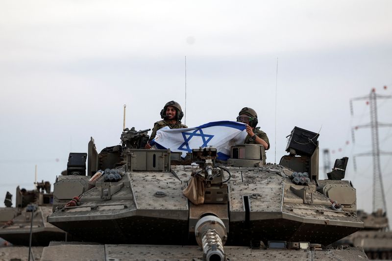 &copy; Reuters. Israeli soldiers hold an Israeli flag while in a tank near Israel's border with the Gaza Strip, in southern Israel, October 12, 2023. REUTERS/Ronen Zvulun