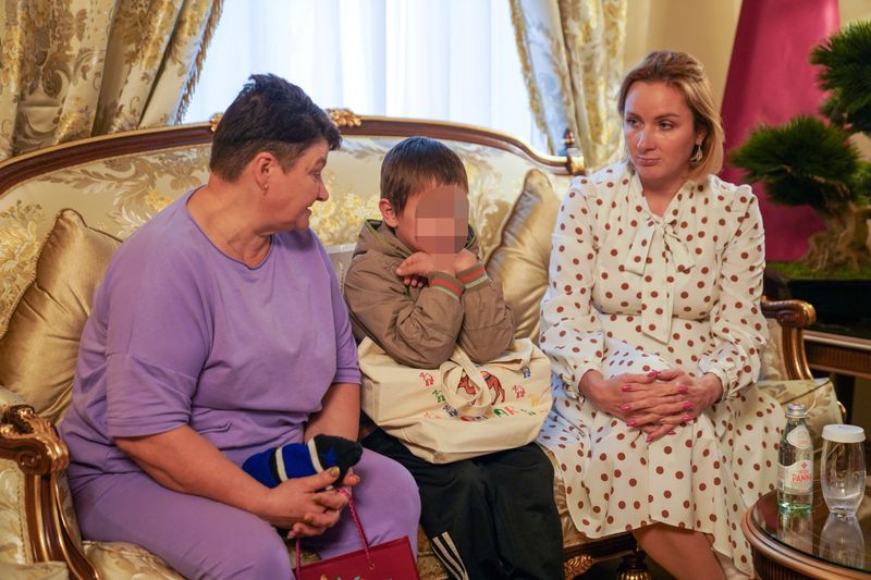 &copy; Reuters. Un niño ucraniano de 7 años, que es el primer niño liberado bajo un nuevo mecanismo que Qatar ha establecido con el objetivo de repatriar a los niños de Rusia a Ucrania, está sentado junto a su abuela (I) y la Comisionada de Rusia para los Derechos d
